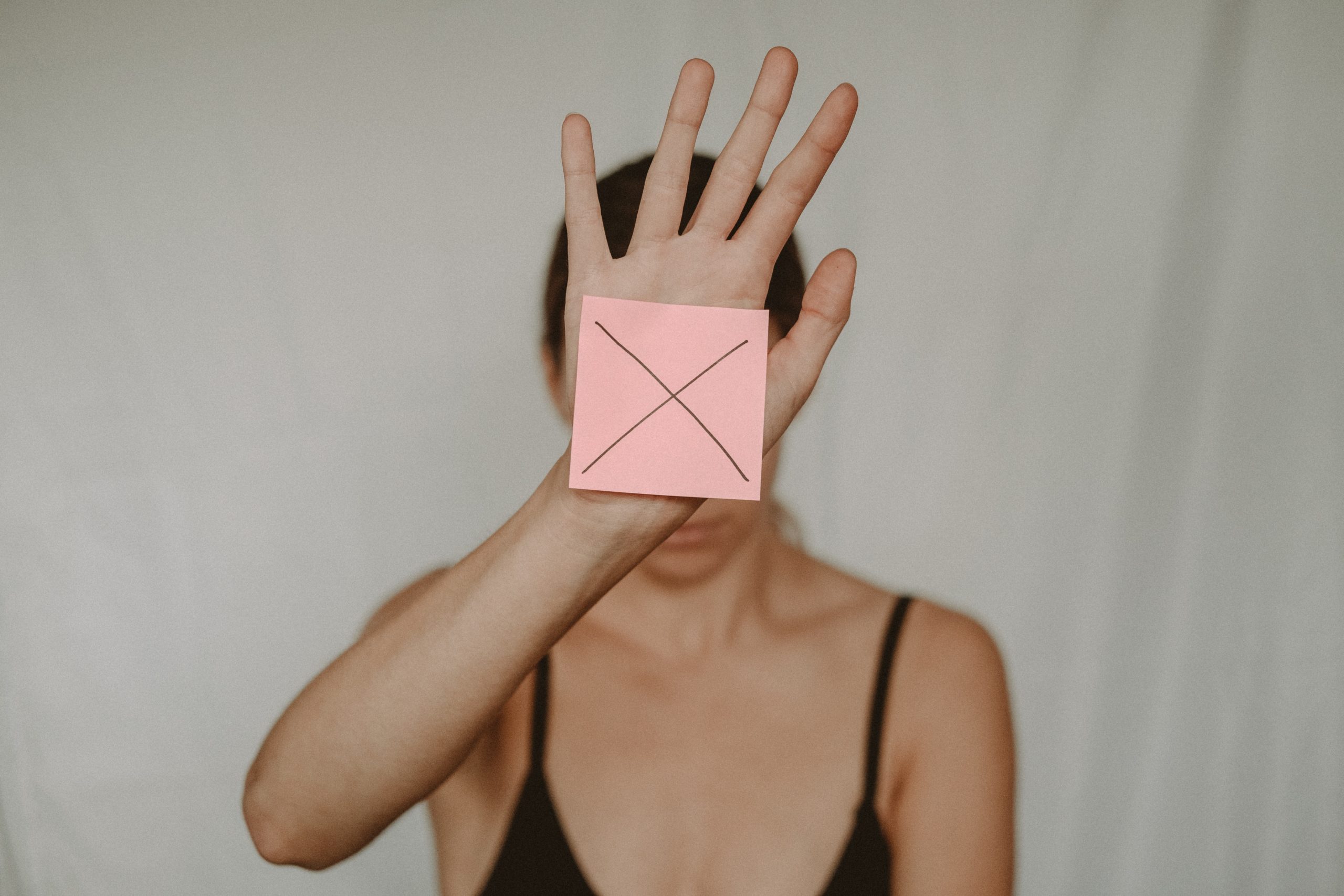 woman holds note in front of face with 'x' on it